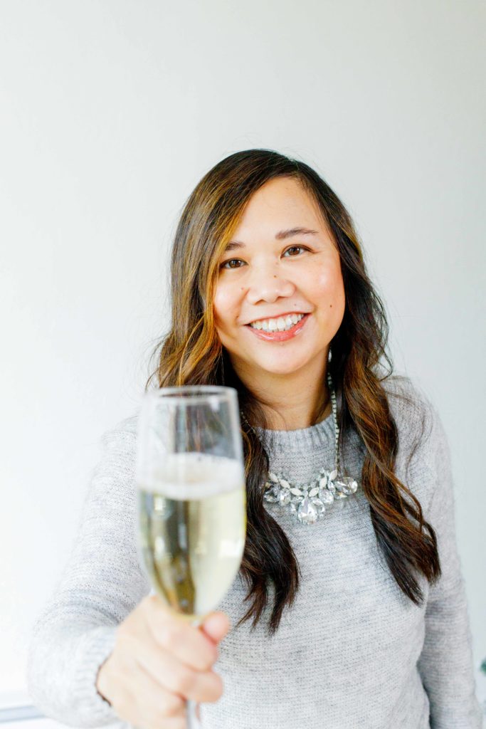 woman smiling while holding out a filled champagne glass in a New Years cheer.